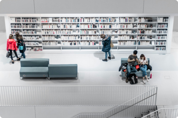 Modern library with white bookshelves, seating areas, and people reading or walking